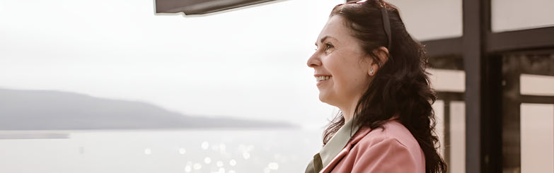 A woman with a bright smile looks out over the calm water, embodying a sense of peace and contentment in the moment.